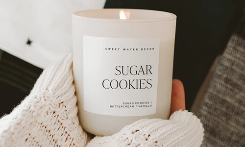 Sweet Water Decor Sugar Cookies candle held beside a cozy knit blanket