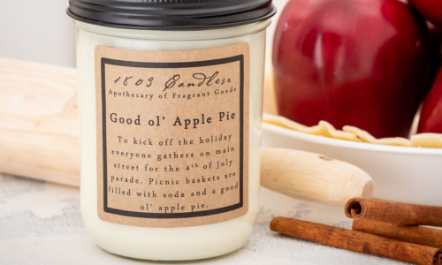 1803 Candles Good Ol' Apple Pie Lifestyle Image 1803 Candles Good Ol' Apple Pie candle displayed with fresh apples and baking-inspired decor.