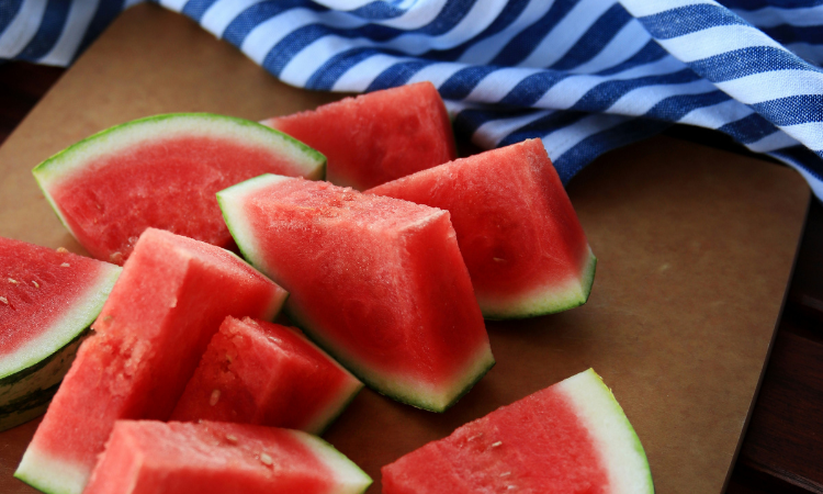 Fresh watermelon slices on a wooden board with a blue and white striped towel